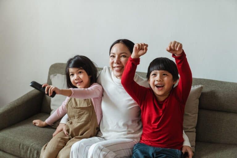 two children sitting beside their mother and cheering at the tv