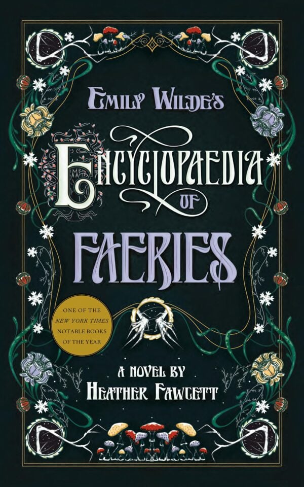 A woman in her 30s sits at a cluttered wooden desk in a study, deeply focused on her work. Emily Wildes Encyclopaedia of Faeries by Heather Fawcett