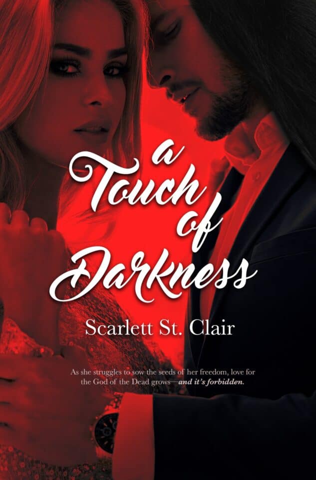 A young woman stands in a dimly lit underground cavern, surrounded by rugged rock formations and torchlight. A Touch of Darkness