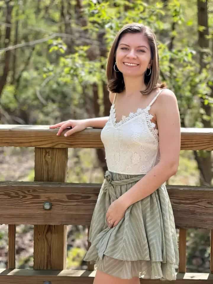 The Crush Dictionary & Recipe Book by Brianna Daus: A Guide to Crushes & Desserts 3 Elegant woman smiling outdoors on a wooden bridge in a natural forest setting, wearing a white lace camisole and a layered skirt for a casual yet chic look.