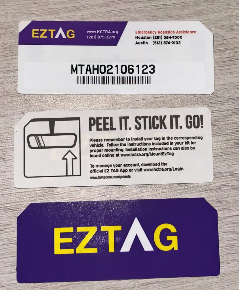 A middle-aged man applies an EZ Tag sticker inside his cluttered car while parked near a toll booth. EZTAG vehicle reminder tag for roadside assistance, featuring barcode, contact info, installation instructions, and peel-and-stick design for easy vehicle identification.