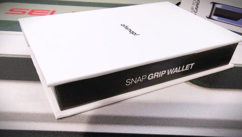 Sleek white and black snap grip wallet packaging on a white surface, highlighting modern wallet design, portability, and minimalist style.