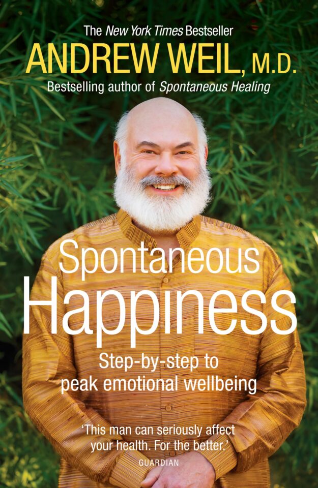 Spontaneous Happiness Book Review: Dr. Andrew Weil's 7 Holistic Paths to Joy 2 A smiling senior man with a white beard wearing a yellow traditional shirt, standing outdoors with green foliage in the background, promoting mental wellness and emotional wellbeing.