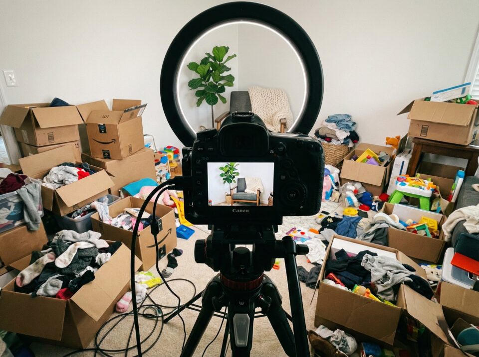 A camera captures a messy toy room filled with open boxes of children's clothes, toys, and scattered items, highlighting organizing challenges.