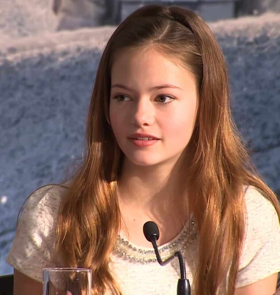 A young woman with red hair and fair skin speaking confidently during an interview or panel discussion, with a rocky or outdoor setting behind her.