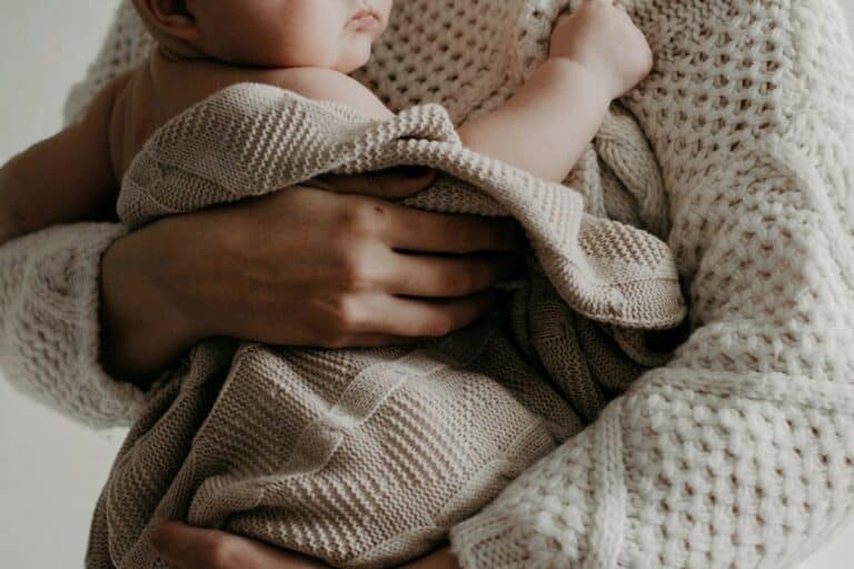 Close-up of mother holding her newborn, emphasizing tenderness and bonding in early motherhood. Warm, cozy tones highlight the love and care in this special moment.