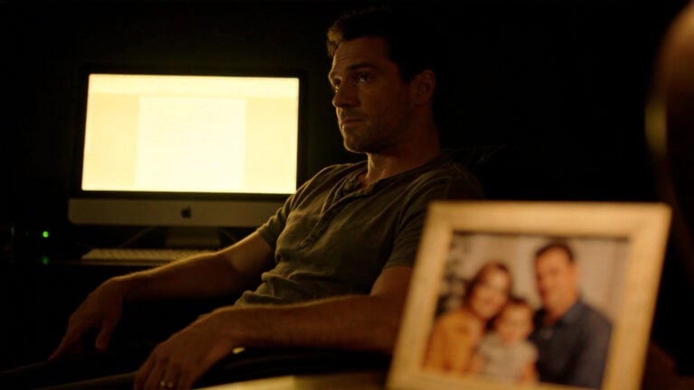 Man in a dimly lit room with a computer and framed photo, emphasizing privacy for adult games and personal boundaries.