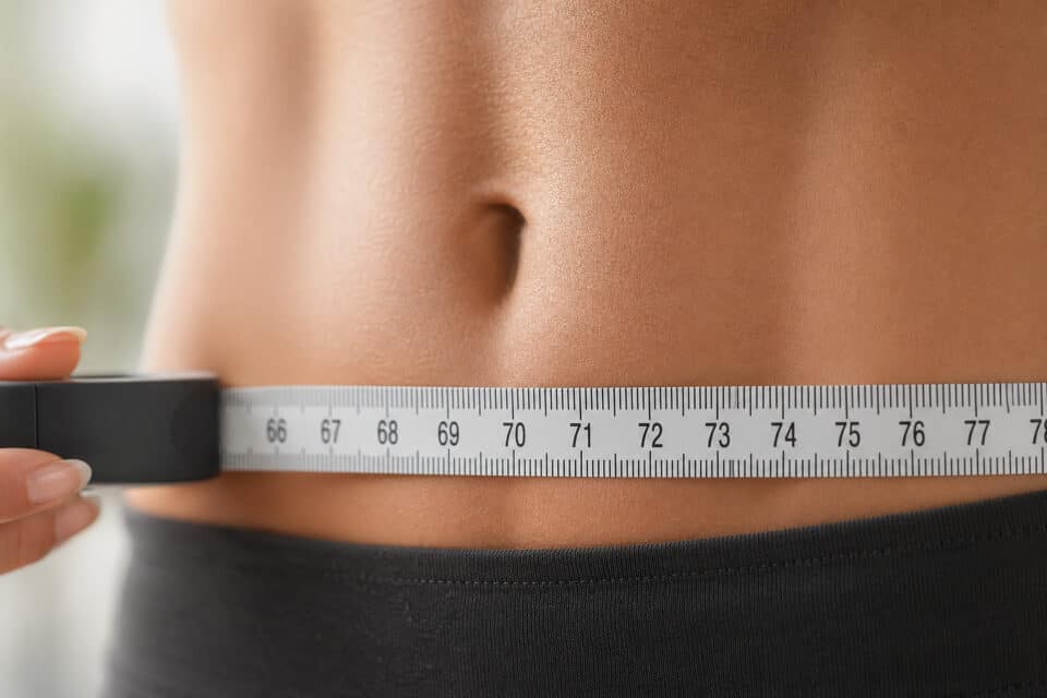 Close-up of a person measuring their waist with a tape measure, emphasizing fitness, health, and body measurement concepts.