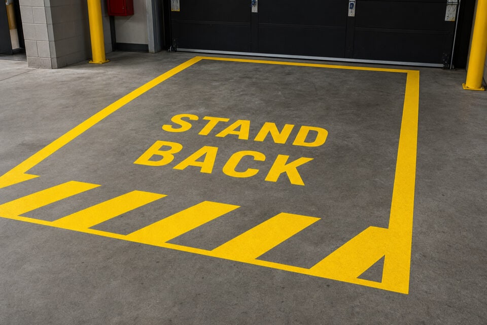 Stop Kids Using the Garage Door: Beyond the 60-Inch Rule 9 Bright yellow 'STAND BACK' safety warning painted on concrete floor in parking garage to ensure social distancing and safety.