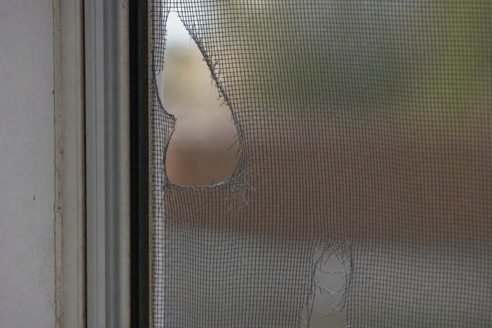 How to Childproof Windows: The 4-Inch Rule and Hardware That Actually Keeps Kids Safe 2 Close-up of a damaged window screen with a large tear and holes, showing the screen mesh and window frame.