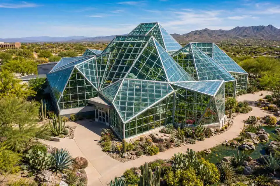 San Antonio Botanical Garden: Is a 38-Acre Walking Tour Worth It? 3 Modern glass house with geometric design in desert setting, surrounded by cacti and desert plants, with mountains in the background.
