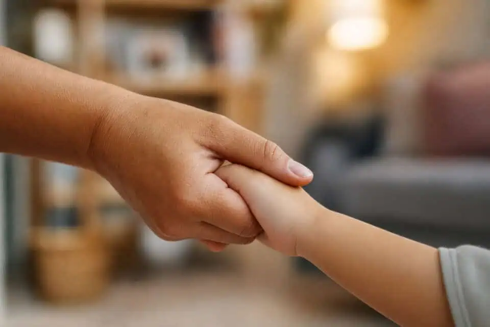 How to Be a Good Mom by Hitting the 70% Rule, Not 100% 7 A caring adult hand gently holding a child's hand, symbolizing support, trust, and reassurance in a warm, cozy home setting.