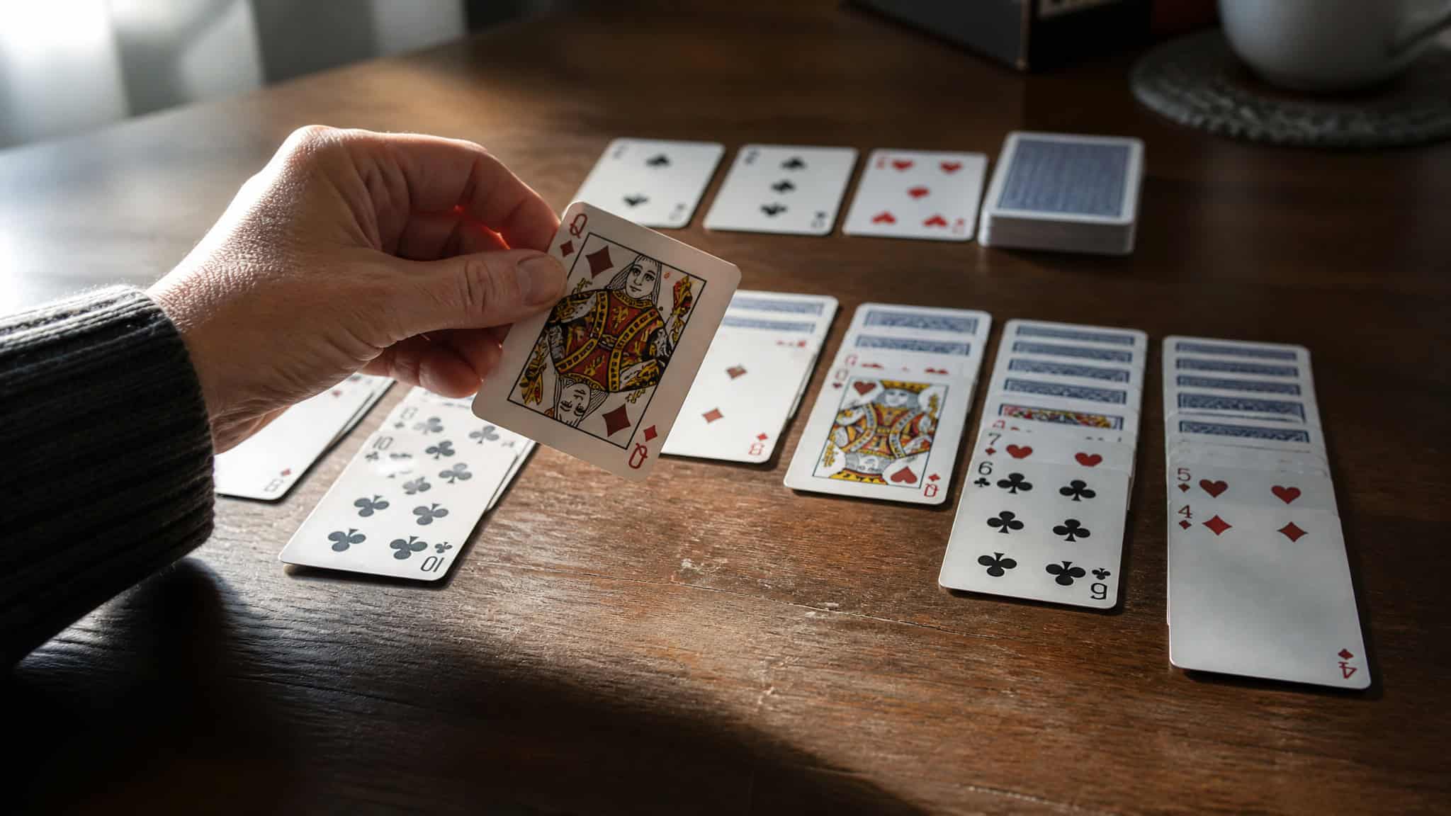 How to Win Solitaire Strategy: Flip Hidden Cards First 3 Hand placing a card from the deck onto a solitaire tableau, showing strategic deck use.