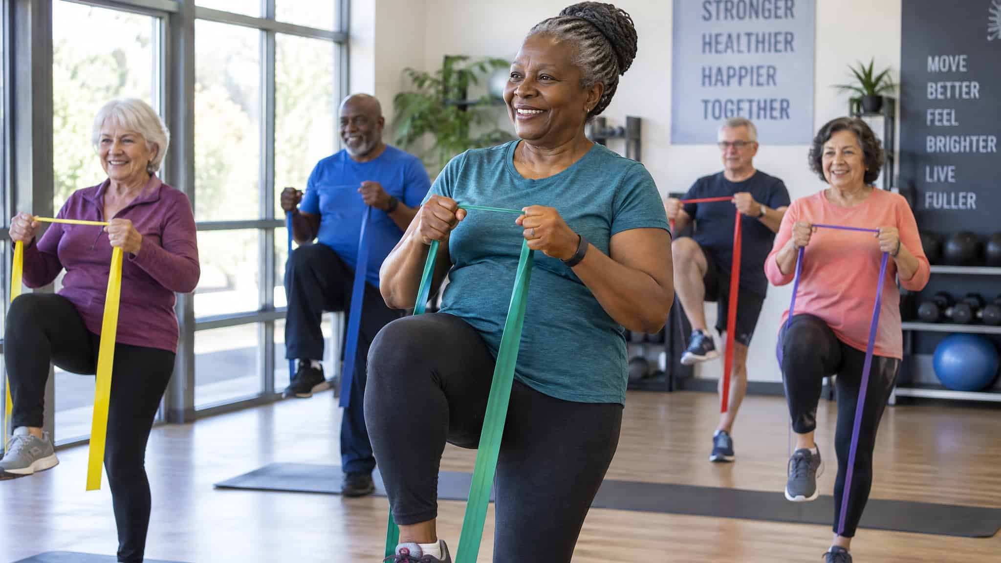 Women Trending Workout Styles for 2026, Ranked by Data — Not TikTok 3 Adults over 55 in a low-impact group class with resistance bands, showing active aging fitness programs
